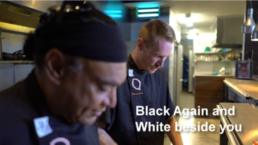 Two men in conversation indoors, one wearing a bandana, with subtitles.